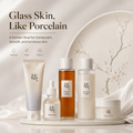 Five Korean beauty products arranged on a white tray against a soft cream background with draped fabric and a decorative plate. Text at the top reads 'Glass Skin, Like Porcelain' with smaller descriptive copy and icons for Hydrate, Glow, and Refine.
