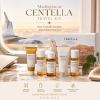 Madagascar Centella Travel Kit by SKIN1004 displayed on a marble surface with an airplane window view in the background. The set includes a white box, a gold tube, a white dropper bottle, a white tube, and a small amber bottle, with travel icons at the bottom.